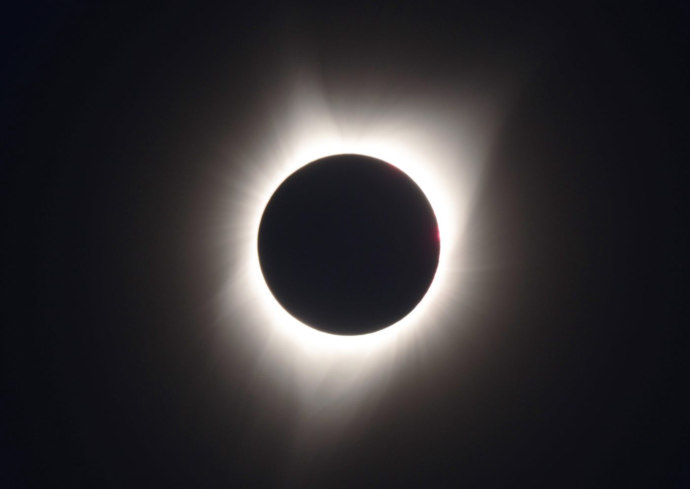 Total solar eclipse showing the Sun's corona around the dark disc of the Moon, with red solar prominences visible at the edge